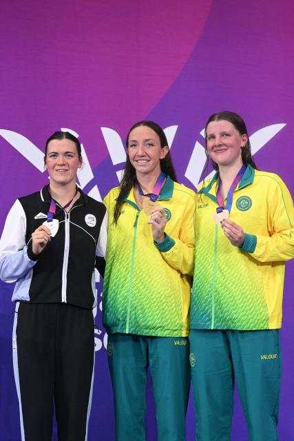 Silver medallist New Zealand's Erika Fairweather (L), gold medallist Australia's Lani Pallister (C) and bronze medallist Australia's Molly Walker celebrate during the medal ceremony for the Women's 1500m Freestyle at the swimming event at the Tollcross International Swimming Centre in Glasgow, on day three of the Commonwealth Games in Glasgow, Scotland, on July 26, 2026. (Photo by Oli SCARFF / AFP)