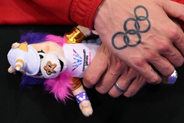 Wales' Matt Richards holds his 'Finnie' mascot next to an olympic ring tattoo during the medal ceremony for the Men's 4 x 200m Freestyle Relay at the swimming event at the Tollcross International Swimming Centre in Glasgow, on day three of the Commonwealth Games in Glasgow, Scotland, on July 26, 2026. (Photo by Oli SCARFF / AFP)