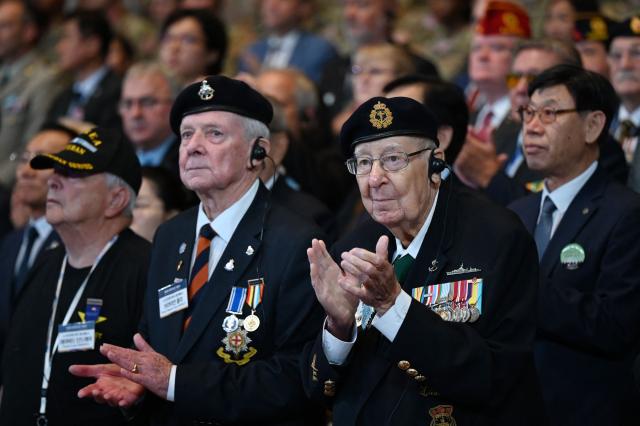 Korean War veterans Andrew Barber (R) of Canada and Brian Morley (L) of Britain applaud during a national ceremony for the Korean War UN Veterans Day in Seoul on July 27, 2026. (Photo by GREG BAKER / AFP)