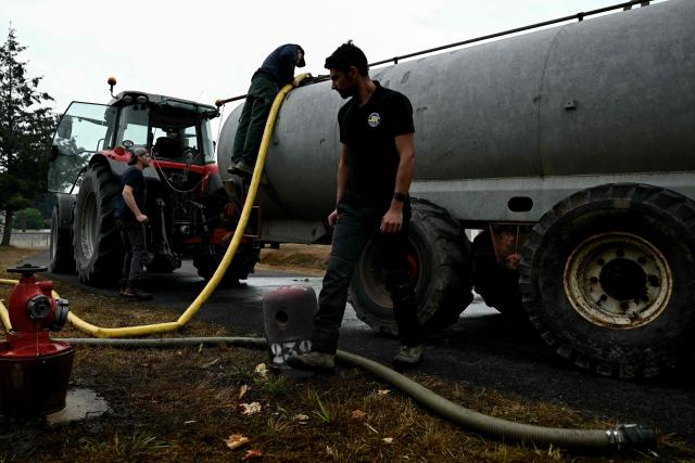 Farmers fill tanks with water to help firefighters battle the fire in Blagon, west of Bordeaux, on July 27, 2026, during wildfires in the Gironde region, southwestern France. Firefighters battled massive blazes tearing through forests across France on July 27, as authorities warned of a fresh heatwave set to engulf the scorched French wine-growing region around the major city of Bordeaux. (Photo by Philippe Lopez / AFP)