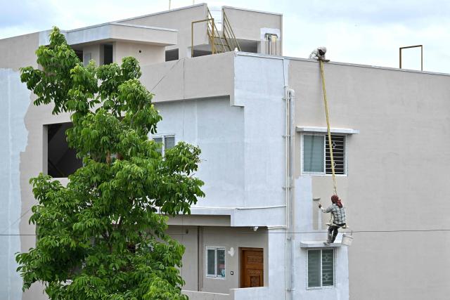 A worker suspended by a rope paints the exterior wall of a newly constructed residential building as fellow worker assists him from the rooftop in Bengaluru on July 27, 2026. (Photo by Idrees MOHAMMED / AFP)