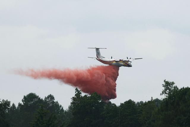 This photograph shows a Bombardier Dash 8 Q400 MR aircraft (R) dropping fire retardant over a forest near Marcheprime, some 30km from Bordeaux, on July 27, 2026, as a wildfire rages through the forest in Gironde, southwestern France. A massive wildfire in France's Gironde department, home to Bordeaux, remained "broadly stable overnight," the local authority said on July 27, 2026. "The situation remained broadly stable overnight, with no major developments. Security and emergency services remain fully mobilised and are continuing their operations on the ground," the local authority said in a statement. (Photo by Alain JOCARD / AFP)