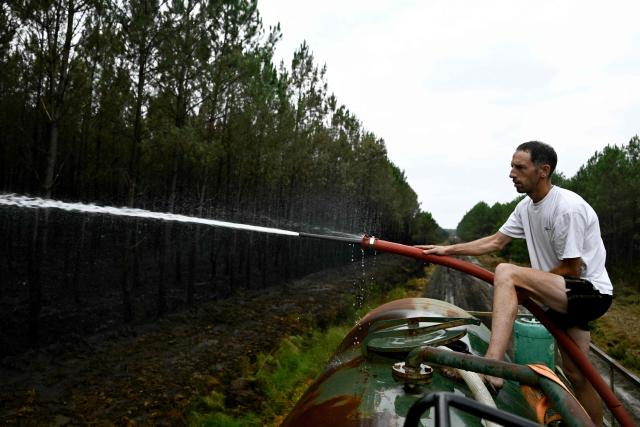 A farmer sprays water on hotspots to help firefighters battle the wildfire in Saint-Jean-d'Illac, west of Bordeaux, on July 27, 2026, during wildfires in the Gironde region, southwestern France. Firefighters battled massive blazes tearing through forests across France on July 27, as authorities warned of a fresh heatwave set to engulf the scorched French wine-growing region around the major city of Bordeaux. (Photo by Philippe Lopez / AFP)