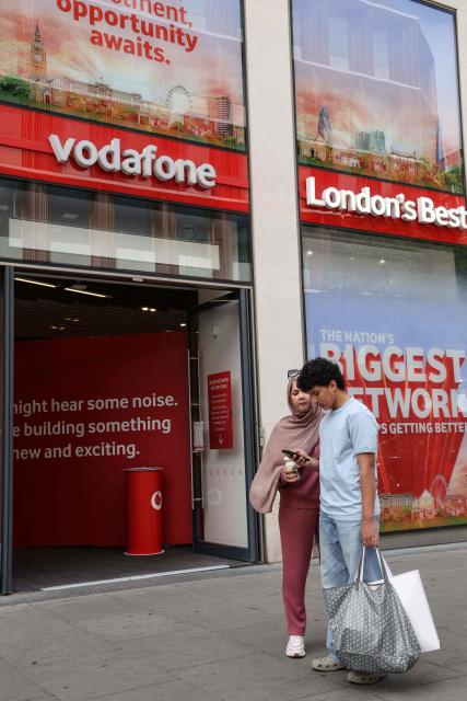 A couple stand outside a shop for British telecommunications group Vodafone in central London on July 27, 2026. Vodafone announced on July 27 a nearly 10 percent increase in revenue for the first quarter and raised its forecasts. (Photo by Adrian DENNIS / AFP)