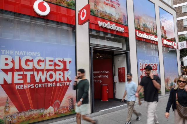 Pedestrians walk past a shop for British telecommunications group Vodafone in central London on July 27, 2026. Vodafone announced on July 27 a nearly 10 percent increase in revenue for the first quarter and raised its forecasts. (Photo by Adrian DENNIS / AFP)