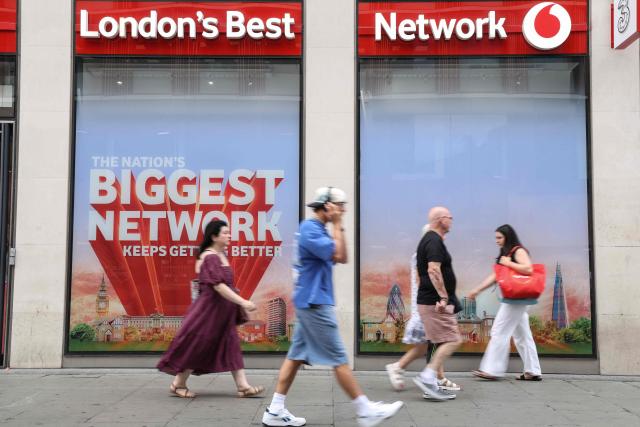 Pedestrians walk past a shop for British telecommunications group Vodafone in central London on July 27, 2026. Vodafone announced on July 27 a nearly 10 percent increase in revenue for the first quarter and raised its forecasts. (Photo by Adrian DENNIS / AFP)