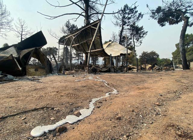 A trail of molten metal from a burnt-out vehicle is seen on the ground as charred remains of caravans and tents are seen following a wildfire at the Pantano de Burguillo campsite in El Barraco, 100 kilometres west of Madrid, on July 27, 2026. Spain faces two crucial days to bring raging wildfires under control before weather conditions worsen, authorities said on July 27, 2026, though they were making some progress and planned to start returning evacuees to certain areas. The wildfires that broke out in forested areas around the Spanish capital at the height of the summer holidays have forced some 60,000 people to flee their homes, often with just minutes' notice, leaving pets and medicine behind. (Photo by Roland LLOYD PARRY / AFP)