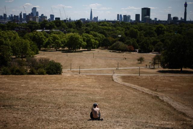 A man sits out on the dry, sun-scorched grass of Primrose Hill, backdropped by the skyline of central London, on July 27, 2026. Temperatures were forecast this to rise back into the 30s for parts of England, following three heatwaves so far over the summer. (Photo by Henry Nicholls / AFP)
