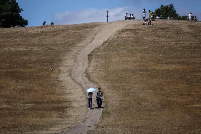 People make their way along a path through the dry, sun-scorched grass of Primrose Hill in central London on July 27, 2026. Temperatures were forecast this to rise back into the 30s for parts of England, following three heatwaves so far over the summer. (Photo by Henry NICHOLLS / AFP)