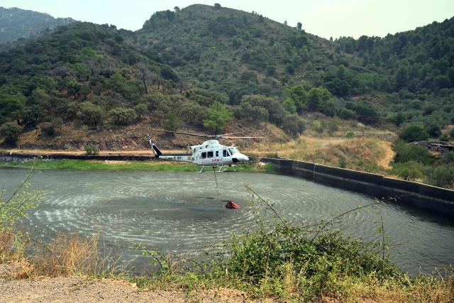 A firefighting helicopter scoops water in the evacuated town of Chovar, 60 kilometres north of Valencia, to use it against the wildfires ravaging the area. Spain faces two crucial days to bring raging wildfires under control before weather conditions worsen, authorities said on July 27, 2026, though they were making some progress and planned to start returning evacuees to certain areas. The fires in the Iberian country have affected an area of 77,000 hectares (190,000 acres) -- nearly the size of New York City -- according to the authorities. Since the start of the year, fires in Spain have ravaged 150,000 hectares and killed 13 people. (Photo by Jose JORDAN / AFP)