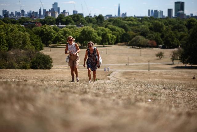 People make their way along a path through the dry, sun-scorched grass of Primrose Hill, backdropped by the skyline of central London, on July 27, 2026. Temperatures were forecast this to rise back into the 30s for parts of England, following three heatwaves so far over the summer. (Photo by Henry Nicholls / AFP)