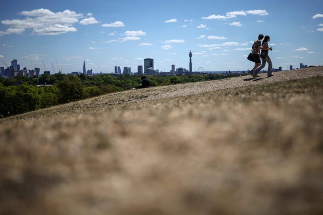 People make their way along a path through the dry, sun-scorched grass of Primrose Hill, backdropped by the skyline (L) of central London, on July 27, 2026. Temperatures were forecast this to rise back into the 30s for parts of England, following three heatwaves so far over the summer. (Photo by Henry Nicholls / AFP)