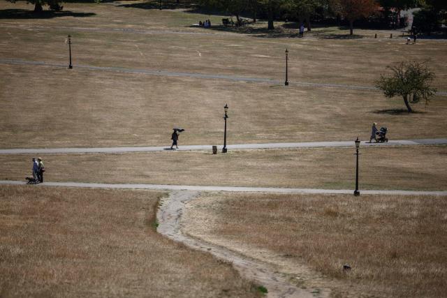People walk along paths through the dry, sun-scorched grass of Primrose Hill in central London on July 27, 2026. Temperatures were forecast this to rise back into the 30s for parts of England, following three heatwaves so far over the summer. (Photo by Henry Nicholls / AFP)