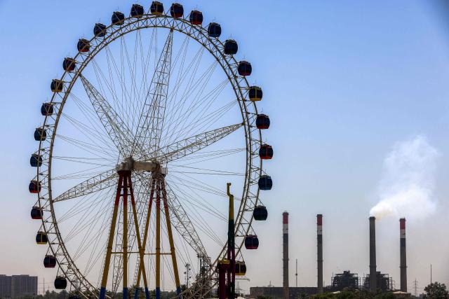 A large Ferris wheel is pictured near the Dora (Daura) Thermal Power Station in the Dora district of southern Baghdad on July 27, 2026. In oil-rich Iraq, many households have just a few hours of state electricity per day, and those who can afford it use private generators to keep fridges and air conditioners running. The country is the second-largest oil producer in the OPEC cartel, but despite its immense oil and gas reserves, it remains dependent on imports to meet its electricity needs. (Photo by AHMAD AL-RUBAYE / AFP)