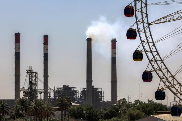 A large Ferris wheel is pictured near the Dora (Daura) Thermal Power Station in the Dora district of southern Baghdad on July 27, 2026. In oil-rich Iraq, many households have just a few hours of state electricity per day, and those who can afford it use private generators to keep fridges and air conditioners running. The country is the second-largest oil producer in the OPEC cartel, but despite its immense oil and gas reserves, it remains dependent on imports to meet its electricity needs. (Photo by AHMAD AL-RUBAYE / AFP)