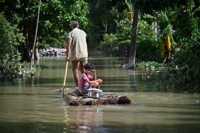 A girl and her grandfather travel on a raft through floodwaters following heavy monsoon rains at a village in Assam's Sivasagar district on July 27, 2026. (Photo by Biju BORO / AFP)