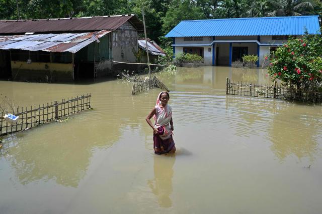 An elderly woman wades through floodwaters near her partially submerged house following heavy monsoon rains at a village in Assam's Sivasagar district on July 27, 2026. (Photo by Biju BORO / AFP)