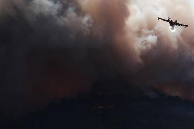 (FILES) A French Civil Security Canadair CL-415 aircraft sprays water on a forest surrounding Cotignac, southeastern France on July 23, 2026 during a wildfire. France has been battered by three heatwaves since May as part of increasingly common extreme weather episodes linked to climate change, causing thousands of excess deaths and fuelling wildfires. (Photo by Thibaud MORITZ / AFP)