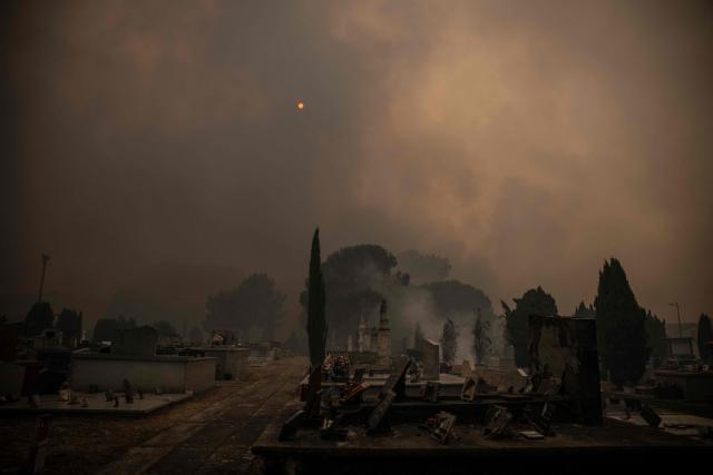(FILES) This photography shows smoke around graves of a cemetary during a wildfire near Lege Cap Ferret, southwestern France on July 23, 2026. France has been battered by three heatwaves since May as part of increasingly common extreme weather episodes linked to climate change, causing thousands of excess deaths and fuelling wildfires. (Photo by JULIEN DE ROSA / AFP)