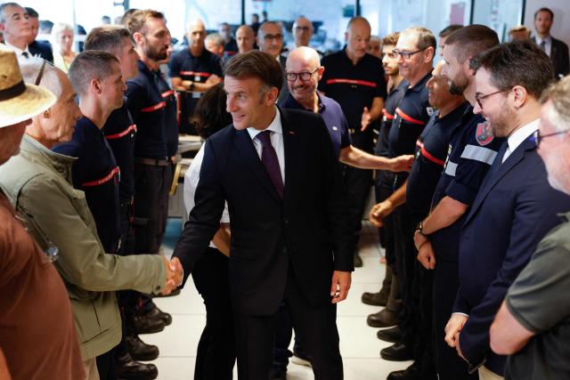 France's President Emmanuel Macron (C) salutes elected officials during a visit to the Departmental Fire and Rescue Operational Center (CODIS) in Bordeaux, following wildfires in the area, southwestern France, on July 27, 2026. France has been battered by three heatwaves since May as part of increasingly common extreme weather episodes linked to climate change, causing excess deaths, drying up rivers and fuelling wildfires. Scientists have long warned that climate change caused by human use of fossil fuels will make periods of drought more intense and longer-lasting, creating the ideal conditions for wildfires. (Photo by Kenzo TRIBOUILLARD / POOL / AFP)
