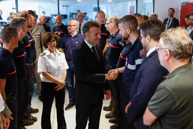 France's President Emmanuel Macron (C) salutes personnel engaged in firefighting efforts during a visit to the Departmental Fire and Rescue Operational Center (CODIS) in Bordeaux, following wildfires in the area, southwestern France, on July 27, 2026. France has been battered by three heatwaves since May as part of increasingly common extreme weather episodes linked to climate change, causing excess deaths, drying up rivers and fuelling wildfires. Scientists have long warned that climate change caused by human use of fossil fuels will make periods of drought more intense and longer-lasting, creating the ideal conditions for wildfires. (Photo by Kenzo TRIBOUILLARD / POOL / AFP)