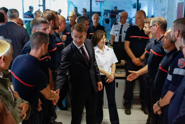 France's President Emmanuel Macron (C) salutes personnel engaged in firefighting efforts during a visit to the Departmental Fire and Rescue Operational Center (CODIS) in Bordeaux, following wildfires in the area, southwestern France, on July 27, 2026. France has been battered by three heatwaves since May as part of increasingly common extreme weather episodes linked to climate change, causing excess deaths, drying up rivers and fuelling wildfires. Scientists have long warned that climate change caused by human use of fossil fuels will make periods of drought more intense and longer-lasting, creating the ideal conditions for wildfires. (Photo by Kenzo TRIBOUILLARD / POOL / AFP)