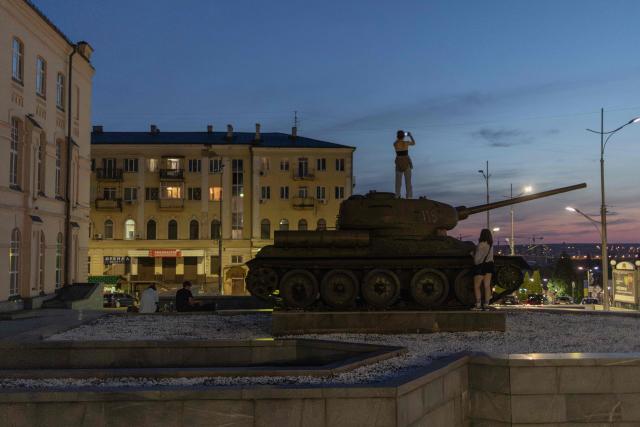 A woman standing atop an exhibited Soviet T-34-85 tank takes a photo of the city's skyline on Constitution Square in the eastern city of Kharkiv on July 27, 2026, amid the Russian invasion of Ukraine. (Photo by Roman PILIPEY / AFP)