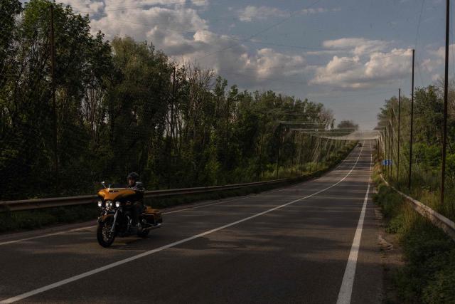 A man rides a motorcycle along a road covered with anti-drone nets, in the eastern Kharkiv region on July 27, 2026, amid the Russian invasion of Ukraine. (Photo by Roman PILIPEY / AFP)