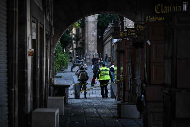 A National Guard member (L) and a police officer secure the crime scene where one man was killed and two others were wounded in an armed attack at Plaza de Santo Domingo in Mexico City's historic center on July 27, 2026. A broad-daylight shooting in Mexico City left one person dead and two others injured just a few blocks from Mexico City's central Zocalo square and the presidential palace, where President Claudia Sheinbaum works and resides. (Photo by Yuri CORTEZ / AFP)
