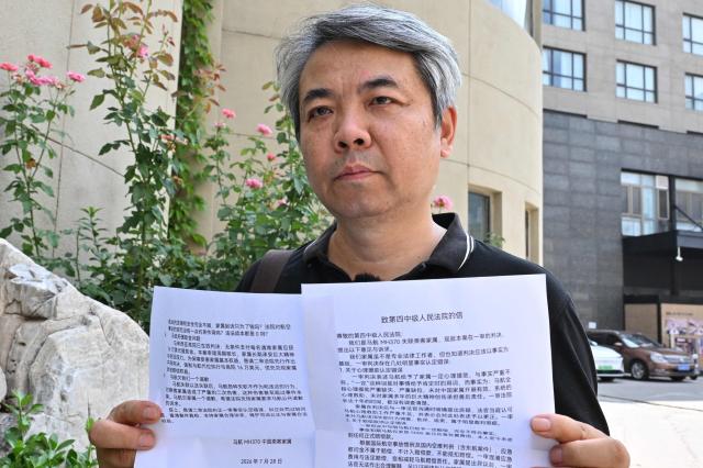 Chinese Jiang Hui, a media coordinator for Chinese passengers families, holds a statement next to the courthouse where a family of the plane MH370 has a hearing in Beijing on July 28, 2026. (Photo by ADEK BERRY / AFP)