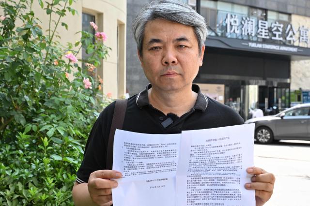 Chinese Jiang Hui, a media coordinator for Chinese passengers families, holds a statement next to the courthouse where a family of the plane MH370 has a hearing in Beijing on July 28, 2026. (Photo by ADEK BERRY / AFP)