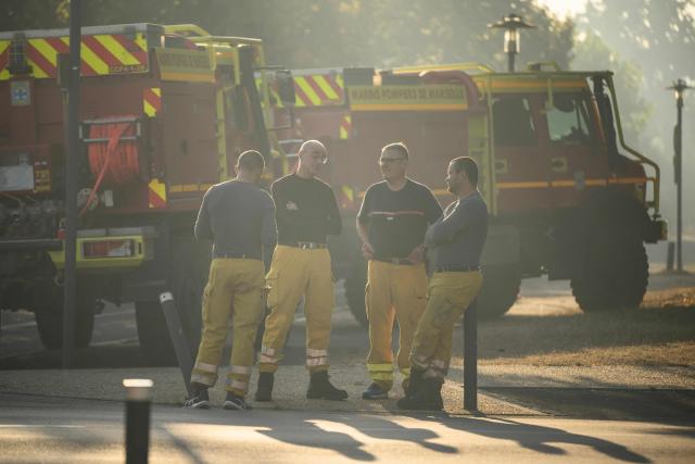 Firefighters stand before vehicles in Lege Cap Ferret on July 28, 2026, during a wildfire in the Gironde region, southwestern France. The expected rise in temperatures raises fears of a further flare-up of the mega-fire that has already ravaged 42,000 hectares in the Gironde; it remained "stabilized" on the morning of July 28, 2026 following a calm night. Forests are catching fire all the more easily because European vegetation and soils have been very dry for monthsa drought exacerbated by climate change and recent exceptional heatwaves. (Photo by Ed JONES / AFP)