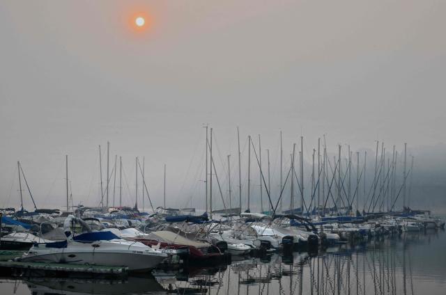 A veiled sun shines through wildfire smoke over a marina in San Juan reservoir after a wildfire ravaged the region in Pelayos de la Presa, 65 kilometres southwest of Madrid, in July 28, 2026. Firefighters in Spain made progress after a "positive night" against wildfires raging west of Madrid that have forced the evacuation of tens of thousands of people, Interior Minister Fernando Grande-Marlaska said today. Spain's government declared a national emergency last week over some of the worst wildfires in the country's history raging in fronts across the Madrid region, Avila province, Toledo and eastern Valencia. (Photo by Miguel RIOPA / AFP)