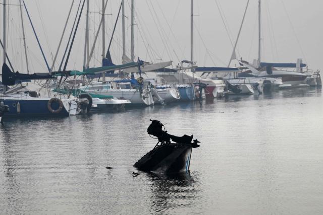 This picture shows a charred boat half-submerged in the San Juan reservoir after a wildfire ravaged the region in Pelayos de la Presa, 65 kilometres southwest of Madrid, in July 28, 2026. Firefighters in Spain made progress after a "positive night" against wildfires raging west of Madrid that have forced the evacuation of tens of thousands of people, Interior Minister Fernando Grande-Marlaska said today. Spain's government declared a national emergency last week over some of the worst wildfires in the country's history raging in fronts across the Madrid region, Avila province, Toledo and eastern Valencia. (Photo by Miguel RIOPA / AFP)