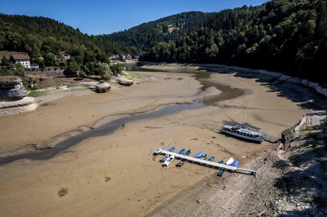 This aerial photograph shows the parched bed of Brenets Lake (Lac des Brenets), part of the Doubs River, a natural border between eastern France and western Switzerland, as central Europe is in a third heatwave since June, in Les Brenets on July 28, 2026. The river has dried up due to a combination of factors, including geological fissures that drain water underground, below-average rainfall and repeated heatwaves. (Photo by Fabrice COFFRINI / AFP)