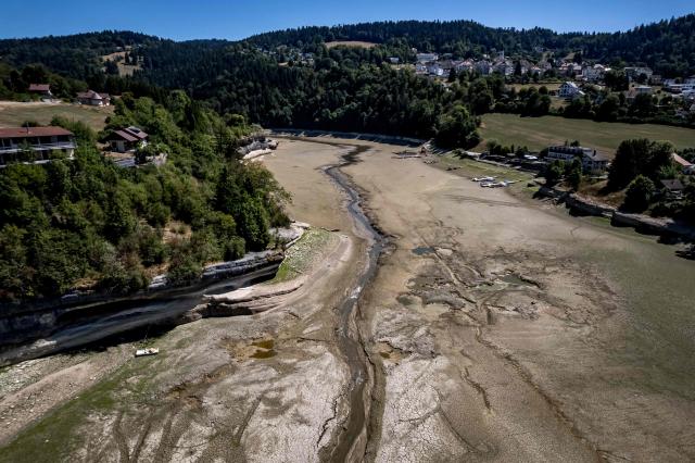This aerial photograph shows the parched bed of Brenets Lake (Lac des Brenets), part of the Doubs River, a natural border between eastern France and western Switzerland, as central Europe is in a third heatwave since June, in Les Brenets on July 28, 2026. The river has dried up due to a combination of factors, including geological fissures that drain water underground, below-average rainfall and repeated heatwaves. (Photo by Fabrice COFFRINI / AFP)