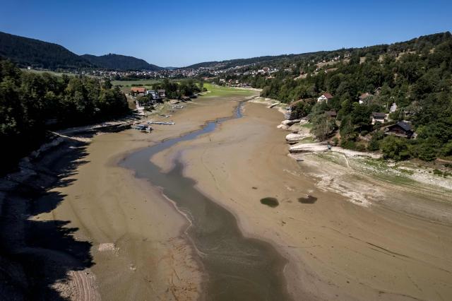 This aerial photograph shows the parched bed of Brenets Lake (Lac des Brenets), part of the Doubs River, a natural border between eastern France and western Switzerland, as central Europe is in a third heatwave since June, in Les Brenets on July 28, 2026. The river has dried up due to a combination of factors, including geological fissures that drain water underground, below-average rainfall and repeated heatwaves. (Photo by Fabrice COFFRINI / AFP)