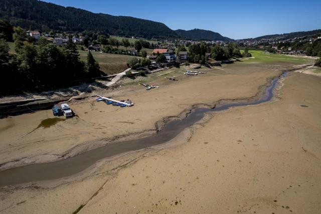 This aerial view shows the parched bed of Brenets Lake (Lac des Brenets), part of the Doubs River, a natural border between eastern France and western Switzerland, as central Europe is in a third heatwave since June, in Les Brenets on July 28, 2026. The river has dried up due to a combination of factors, including geological fissures that drain water underground, below-average rainfall and repeated heatwaves. (Photo by Fabrice COFFRINI / AFP)