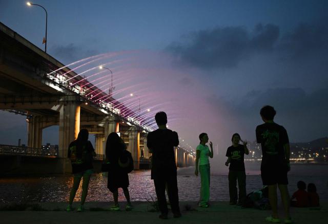 People watch the Moonlight Rainbow Fountain on Banpo Bridge, over the Han River in Seoul on July 28, 2026. (Photo by GREG BAKER / AFP)