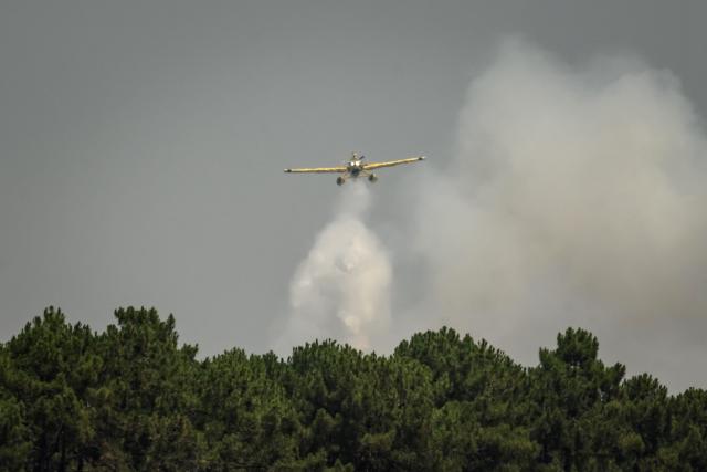 An aircraft flies over smoke rising from a forest fire outside Lege-Cap-Ferret, southwestern France on July 28, 2026. Over the past six days, the wildfire near Bordeaux has ravaged 42,000 hectares (103,000 acres), forced 220,000 people to flee and destroyed 240 houses. Firefighters said on July 28, 2026 the fire had not expanded overnight as they managed to tackle several flareups. (Photo by Ed JONES / AFP)