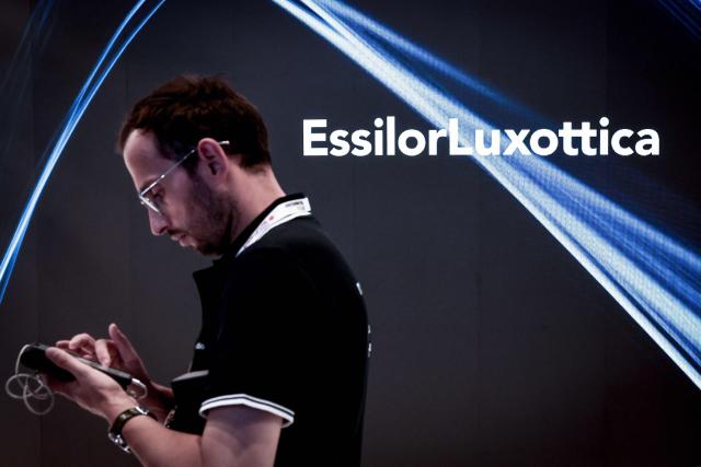 (FILES) A man examines his mobile telephone as he passes by the EssilorLuxottica logo at the 9th edition of the VivaTech technology startups and innovation fair at the Paris Expo Porte de Versailles, in Paris on June 11, 2025. The world’s leading optics company EssilorLuxottica accelerated its growth in the second quarter, on July 28, 2026 despite "a more uncertain global macroeconomic environment," driven by its AI-enabled glasses, whose sales have nearly doubled in the space of a year. (Photo by Thibaud MORITZ / AFP)