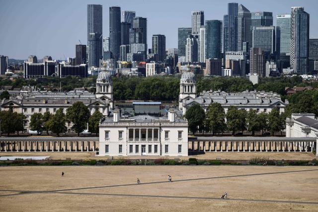 People (bottom) walk across the dried out and yellow grass in Greenwich Park, in front of the Old Royal Naval College (C) and the skyline of Canary Wharf (behind), in south-east London on July 29, 2026. Just over half of England has been declared in drought after "record-low rain and exceptionally high temperatures", the UK government said on July 29. (Photo by Henry NICHOLLS / AFP)