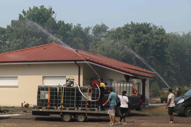 Volunteers use water hoses next to a building amid firefighter operations against a wildfire near Lanton, southwestern France, on July 29, 2026. The return of intense heat on July 29, 2026, and sea winds are fanning the megafire in Gironde, with new flare-ups in places after a second, calmer night that had made it possible to “stabilize” the blaze. Forests catch fire all the more easily because the vegetation and soil have been extremely dry for months, a drought worsened by climate change and the recent exceptional heatwaves. (Photo by Alain JOCARD / AFP)