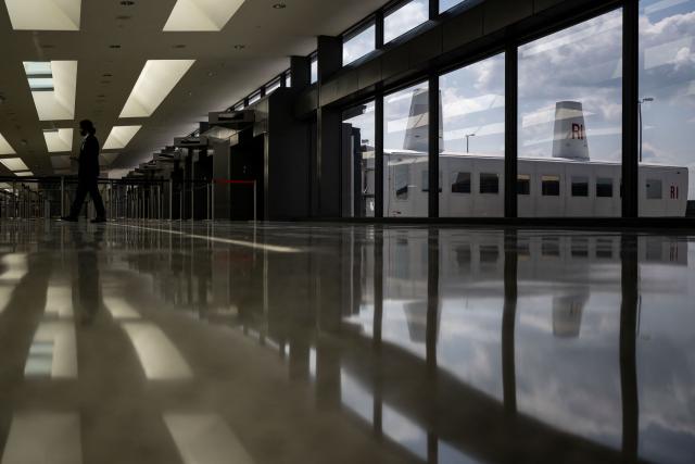 A mobile lounge vehicle (R), colloquially called a "people-mover," is parked at the main terminal at Washington Dulles International Airport (IAD) in Dulles, Virginia, on July 29, 2026. US President Donald Trump is set to unveil on Wednesday a $20 billion plan to rebuild and renovate Washington Dulles International Airport. (Photo by Kent Nishimura / AFP)
