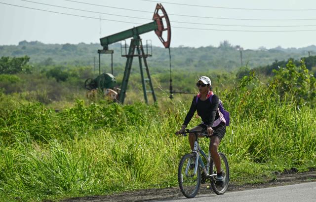 A woman rides past an old oil pump in Boca de Jaruco, Matabeque Province, Cuba on July 29, 2026. Cuba on July 29, 2026, moved to open several key crisis-ravaged sectors of its state-run economy to private firms, as the communist government tries to ease acute shortages resulting from a US energy blockade. (Photo by YAMIL LAGE / AFP)