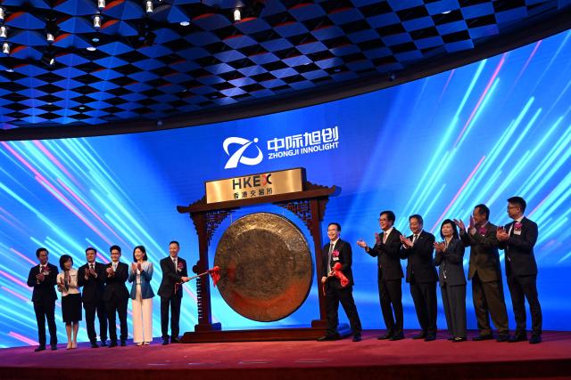 Liu Sheng, Chairman and CEO of Zhongji Innolight (centre R) bangs the gong at the start of trading with his director Wang Xiaodong (centre L) during the launch of the company's initial public offering (IPO) at the Hong Kong Exchanges and Clearing Limited (HKEX) in Hong Kong on July 30, 2026. (Photo by Peter PARKS / AFP)