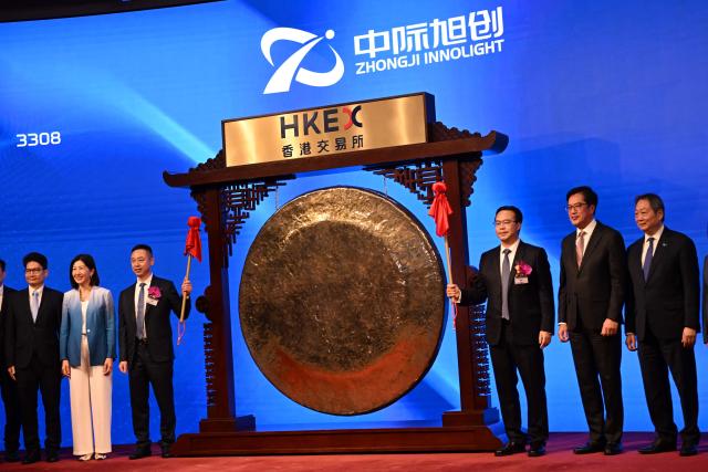 Liu Sheng, Chairman and CEO of Zhongji Innolight (centre R) poses after banging the gong at the start of trading with his director Wang Xiaodong (centre L) during the launch of the company's initial public offering (IPO) at the Hong Kong Exchanges and Clearing Limited (HKEX) in Hong Kong on July 30, 2026. (Photo by Peter PARKS / AFP)