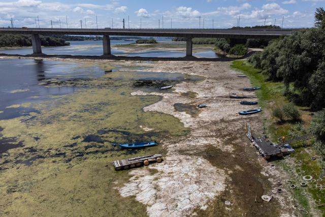 An aerial photograph taken on July 22, 2026 shows boats laying on the dried Danube river bed in front of the Calafat-Vidin bridge, connecting Bulgaria and Romania near the village Antimovo, southeastern Bulgaria. At the Romanian town of Corabia on the banks of the Danube river, some boats are stranded in shallow water full of algae in the touristic port, which lies deserted as ships can no longer dock due to sandbars (Photo by Nikolay DOYCHINOV / AFP)