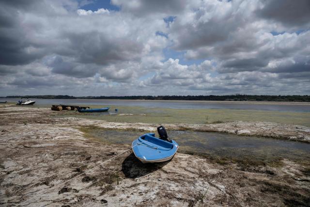 A photograph taken on July 22, 2026 shows a boat laying on the dried Danube river bed in front of the Calafat-Vidin bridge, connecting Bulgaria and Romania near the village Antimovo, southeastern Bulgaria. At the Romanian town of Corabia on the banks of the Danube river, some boats are stranded in shallow water full of algae in the touristic port, which lies deserted as ships can no longer dock due to sandbars (Photo by Nikolay DOYCHINOV / AFP)