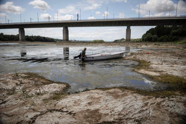 A fisherman tries to move his boat, blocked by algae on the bottom of the Danube river in front of the Calafat-Vidin bridge, connecting Bulgaria and Romania near the village Antimovo, southeastern Bulgaria, on July 22, 2026. At the Romanian town of Corabia on the banks of the Danube river, some boats are stranded in shallow water full of algae in the touristic port, which lies deserted as ships can no longer dock due to sandbars (Photo by Nikolay DOYCHINOV / AFP)